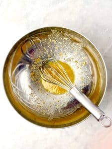 Apple cider vinegar and Dijon slaw dressing being whisked in a glass bowl.