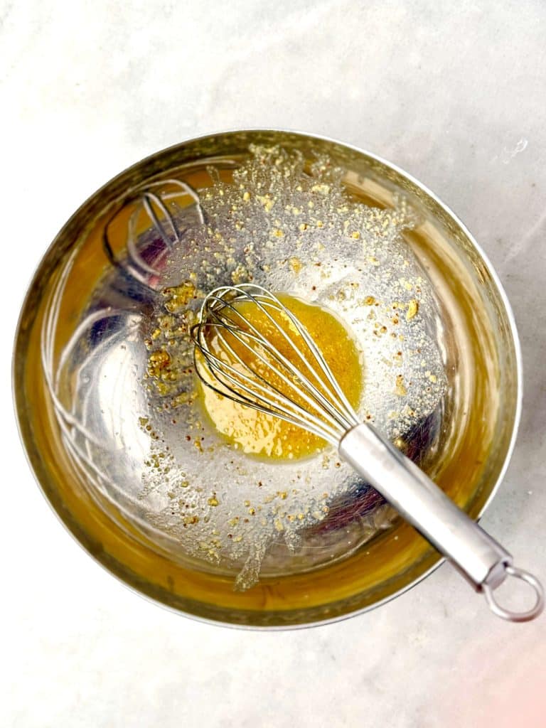 Apple cider vinegar and Dijon slaw dressing being whisked in a glass bowl.