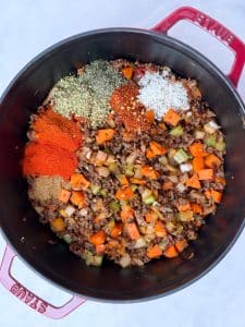 Spices being added to browned ground beef and vegetables in a pot for high-protein unstuffed cabbage soup