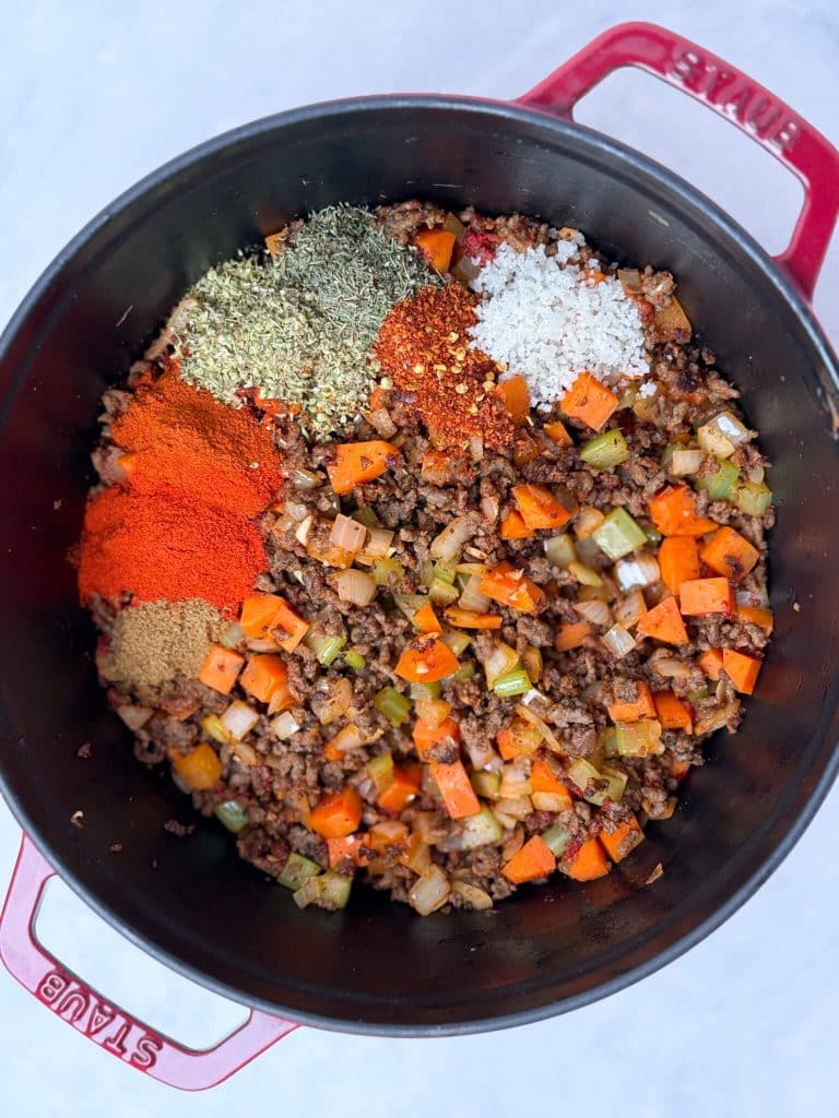 Spices being added to browned ground beef and vegetables in a pot for high-protein unstuffed cabbage soup