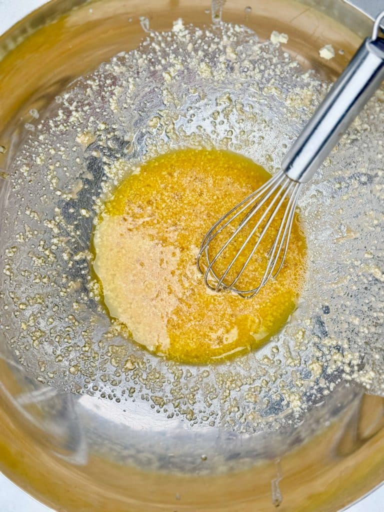 Leon dressing for La Scala dense bean salad recipe made with olive oil, red wine vinegar, Dijon mustard, garlic, and grated parmesan being whisked in a bowl.