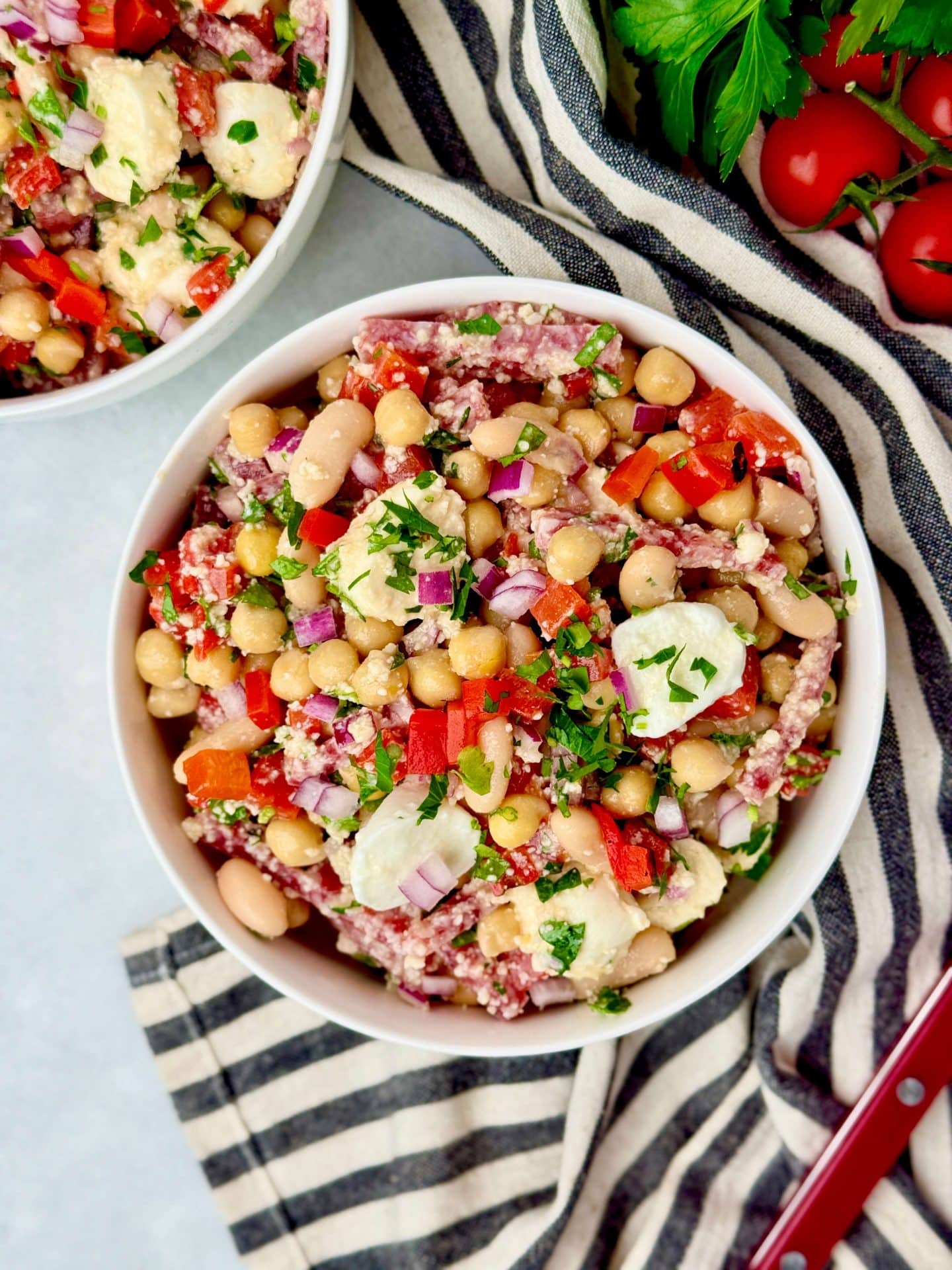 La Scala dense bean salad recipe made with chickpeas, white beans, salami, mozzarella pearls, roasted red peppers, red onion, parsley, and grated parmesan in a white bowl.