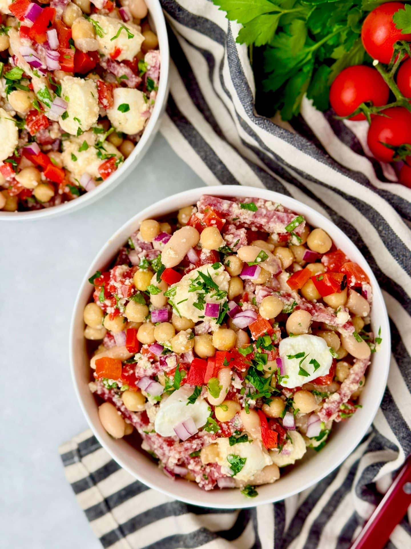 Two bowls of La Scala dense bean salad with Italian salami, creamy mozzarella, chickpeas, cannellini beans, and parmesan tossed in Leon dressing.