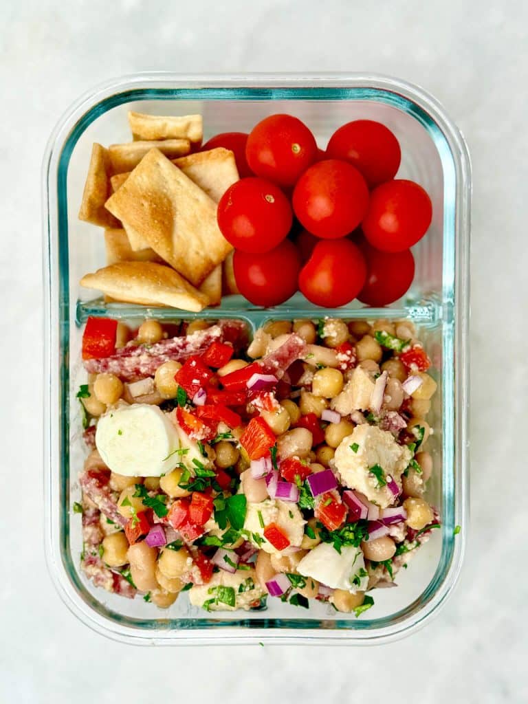 La Scala dense bean salad meal prep with chickpeas, white beans, salami, mozzarella, cherry tomatoes, and crackers in a glass container.