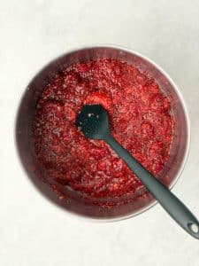 Homemade raspberry chia jam made with frozen raspberries and chia seeds simmering in a saucepan.