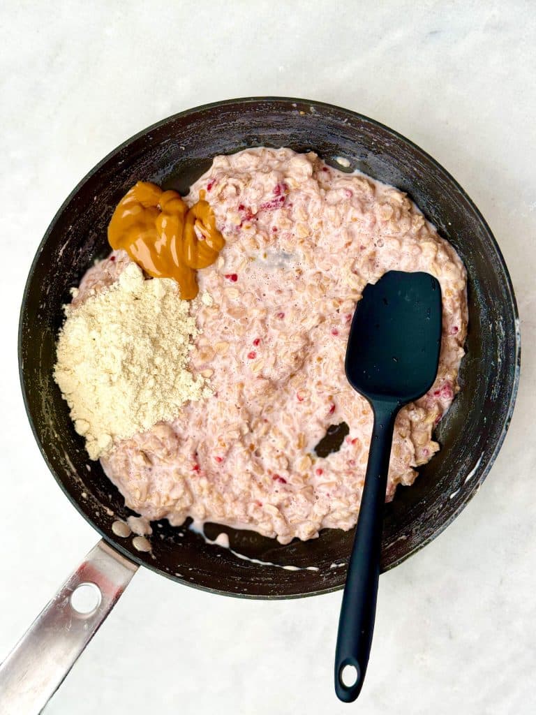 Protein oatmeal in a saucepan with peanut butter and vanilla protein powder being stirred together.