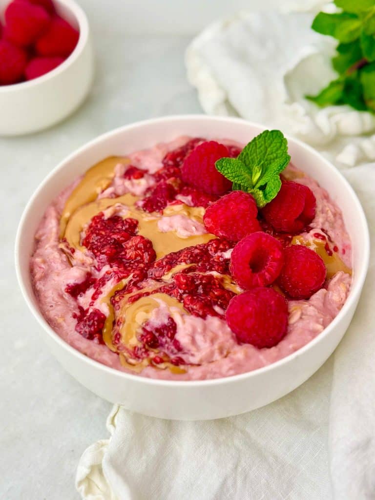 Peanut butter and jelly oatmeal with creamy protein oats, raspberry chia jam, and fresh raspberries.