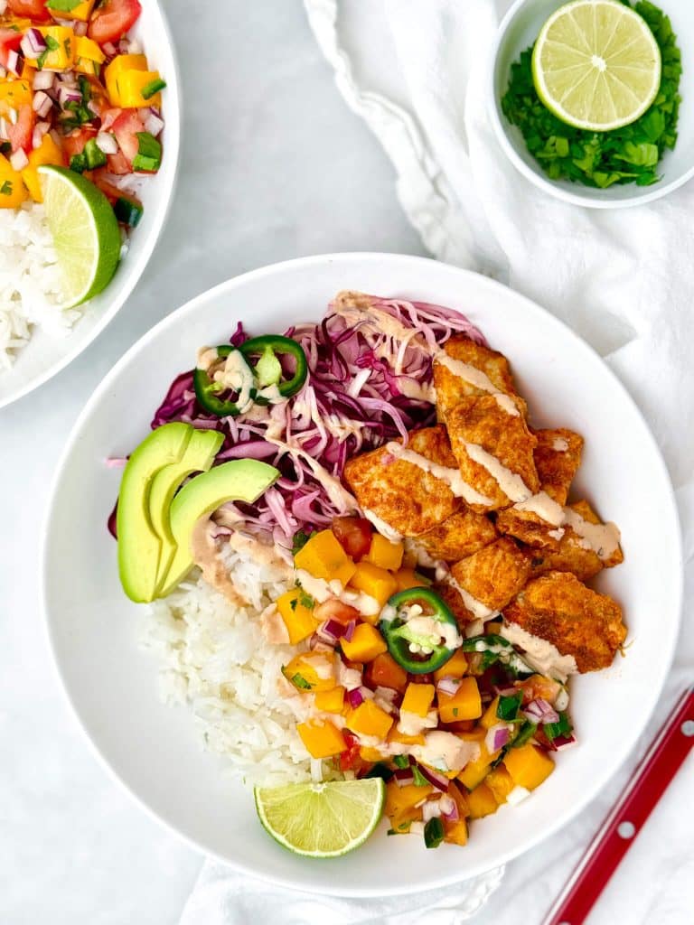 Two air fryer fish taco bowls with rice, mango salsa, red cabbage slaw, avocado, and chipotle crema