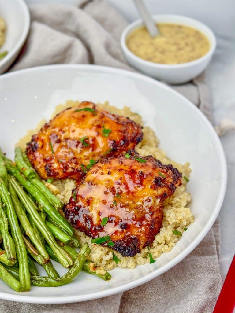 Close up of glazed air fryer honey mustard chicken thighs over quinoa with green beans and fresh parsley