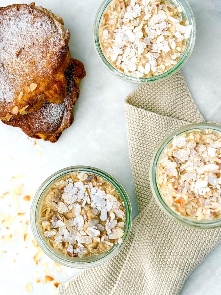 Overhead view of three jars of overnight oats with sliced almonds next to an almond croissant
