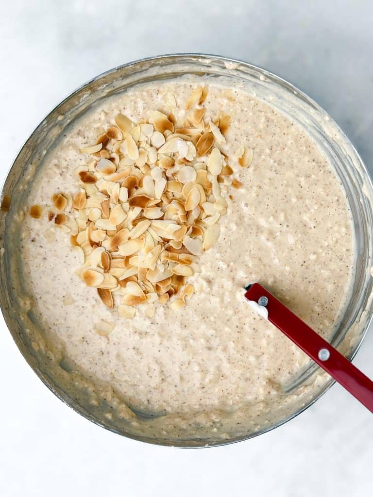 Stirred overnight oat mixture in a glass bowl topped with sliced almonds