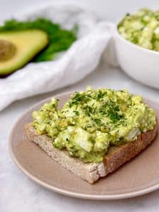 avocado egg salad served on a slice of toast on a pink plate with fresh dill on top