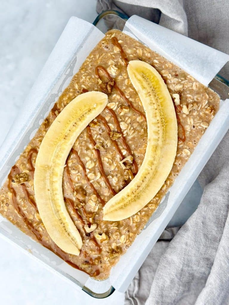Unbaked banana bread oatmeal in a dish topped with banana halves and peanut butter drizzle
