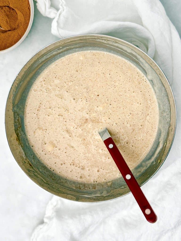banana bread overnight oats base with Greek yogurt, milk, and protein powder blended smooth in a large metal mixing bowl with a red spoon before adding oats