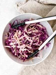 Cabbage slaw with tongs in a white bowl