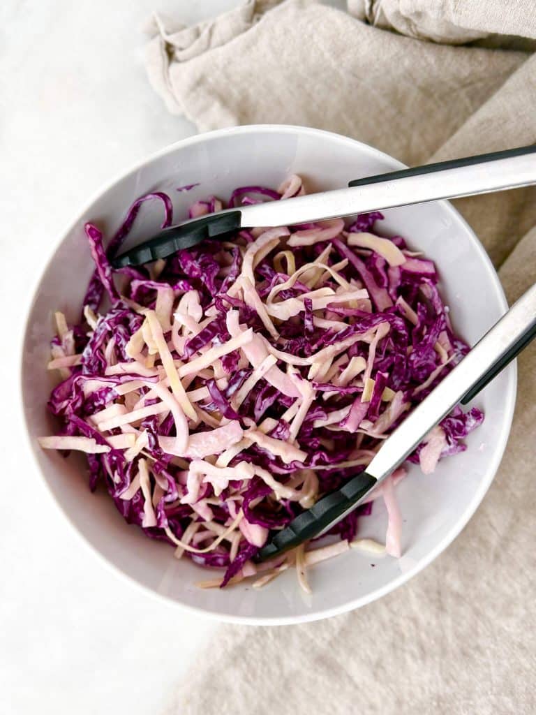 Cabbage slaw with tongs in a white bowl