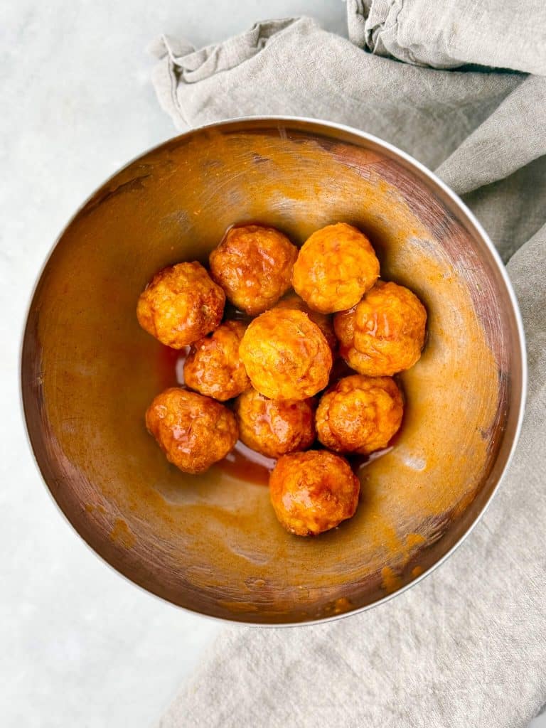 Baked chicken meatballs tossed in buffalo sauce in a mixing bowl