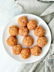 Raw ground chicken meatballs on a white plate before baking