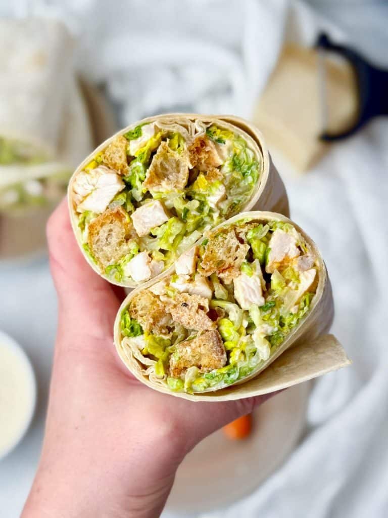 hand holding a high protein chicken caesar wrap cut in half showing romaine chicken croutons and caesar dressing