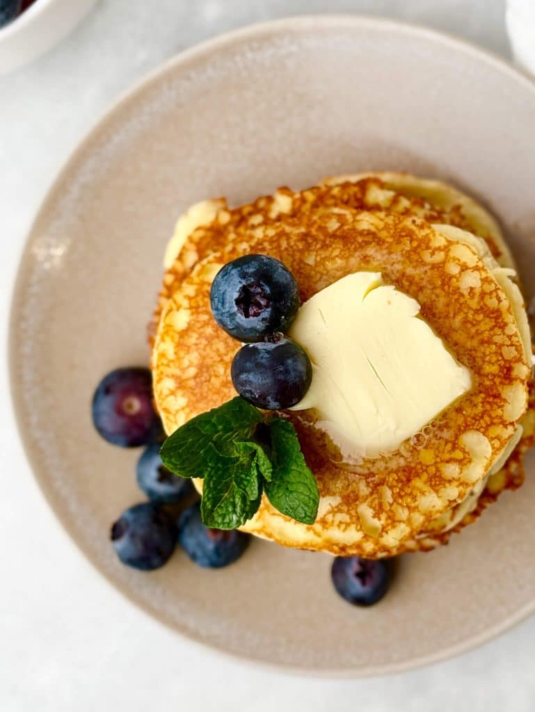 close up overhead view of low carb cottage cheese pancakes with butter and blueberries on a plate