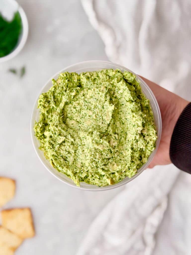 Hand holding a round deli container filled with green goddess chicken salad