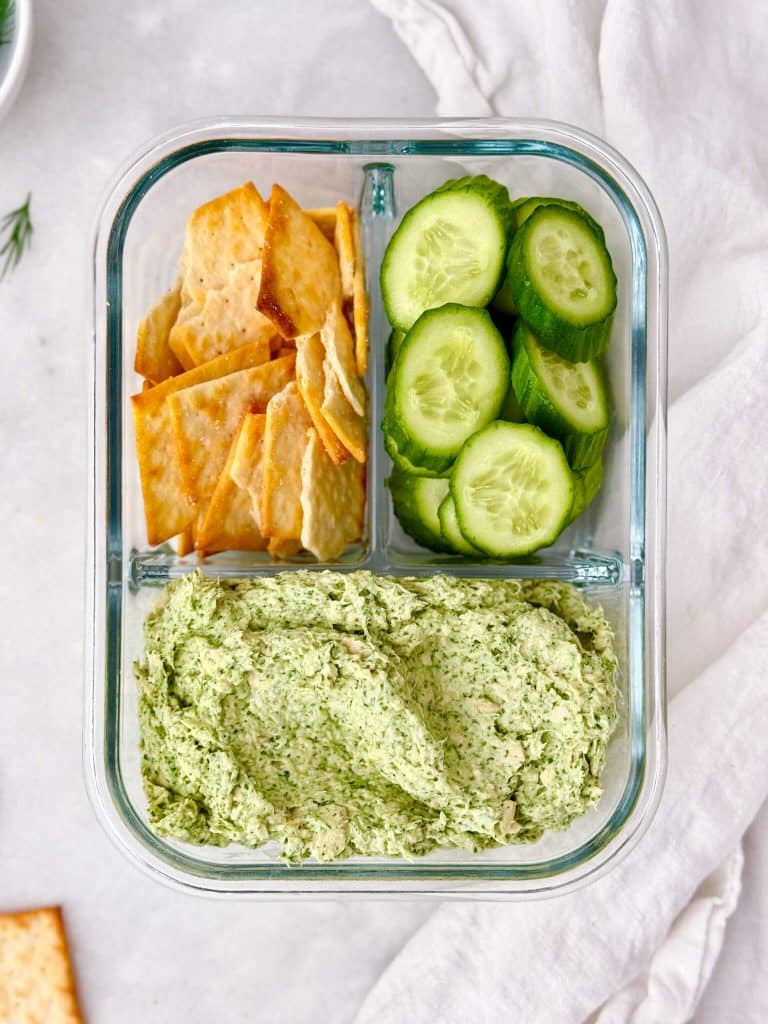 Green goddess chicken salad in a glass meal prep container with pita crackers and sliced cucumbers
