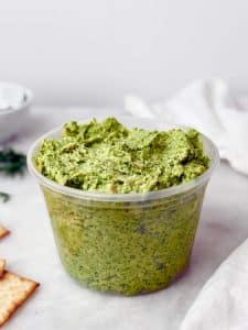 Green goddess chicken salad in a deli container with crackers and fresh herbs.