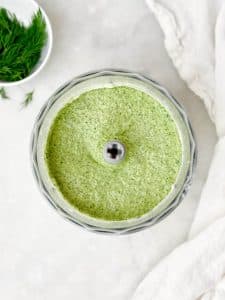 Smooth green goddess dressing blended in a food processor, creamy texture with visible herb flecks