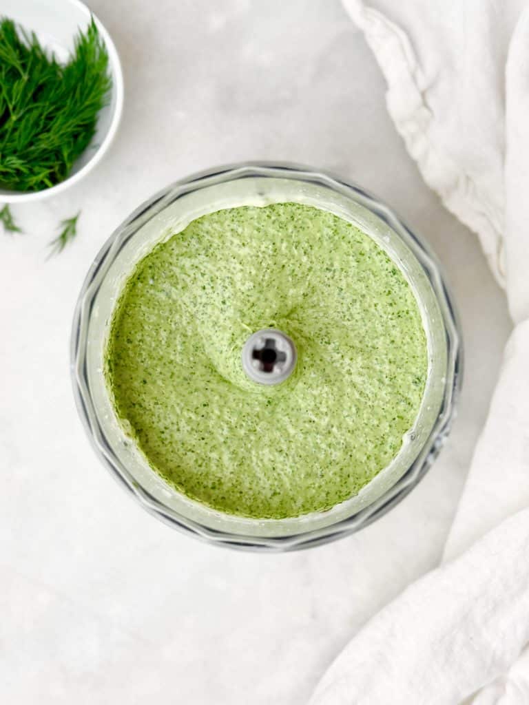 Smooth green goddess dressing blended in a food processor, creamy texture with visible herb flecks