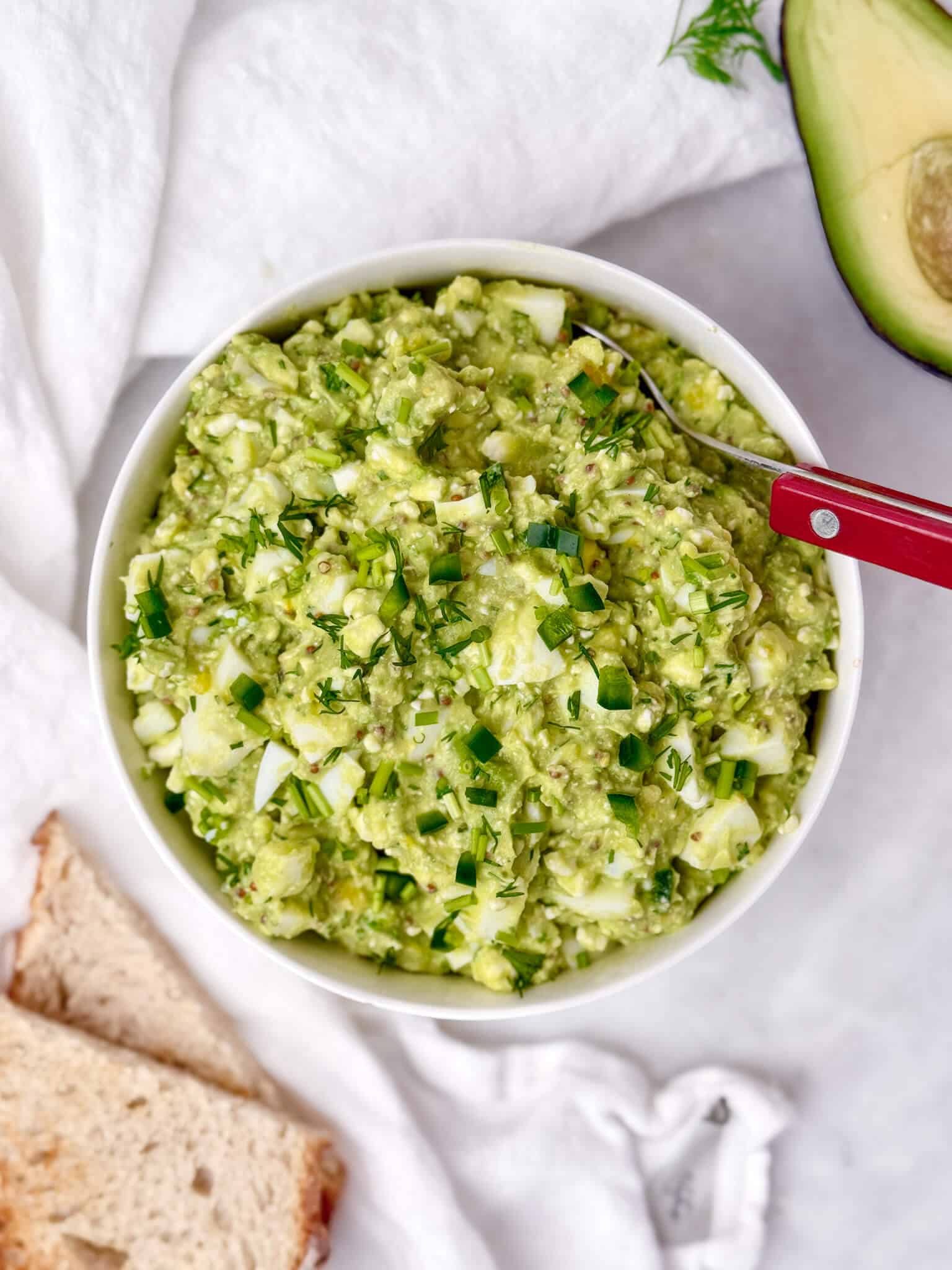close overhead view of high-protein avocado egg salad with chopped chives and dill on top in a white bowl