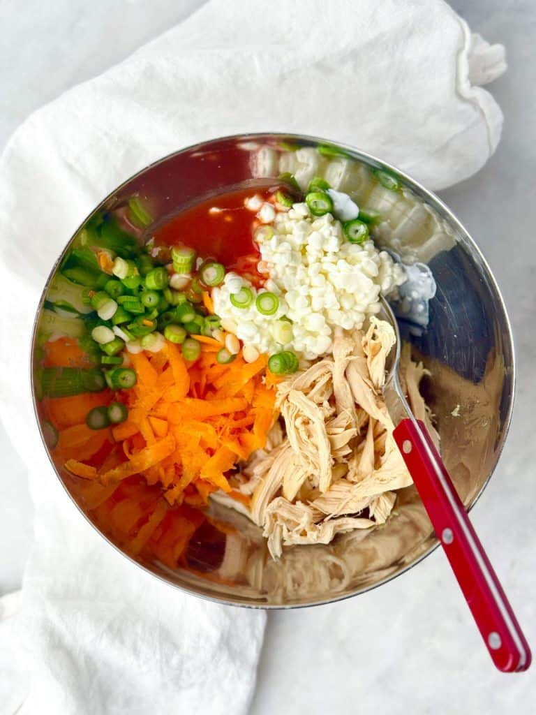high protein buffalo chicken wrap cottage cheese filling with shredded chicken, carrot, green onion, and buffalo sauce in a mixing bowl