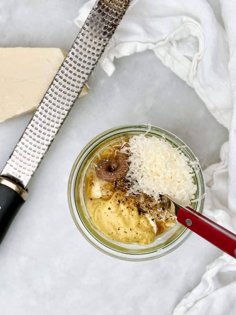 greek yogurt caesar dressing ingredients in a jar with dijon mustard anchovy paste parmesan and a microplane