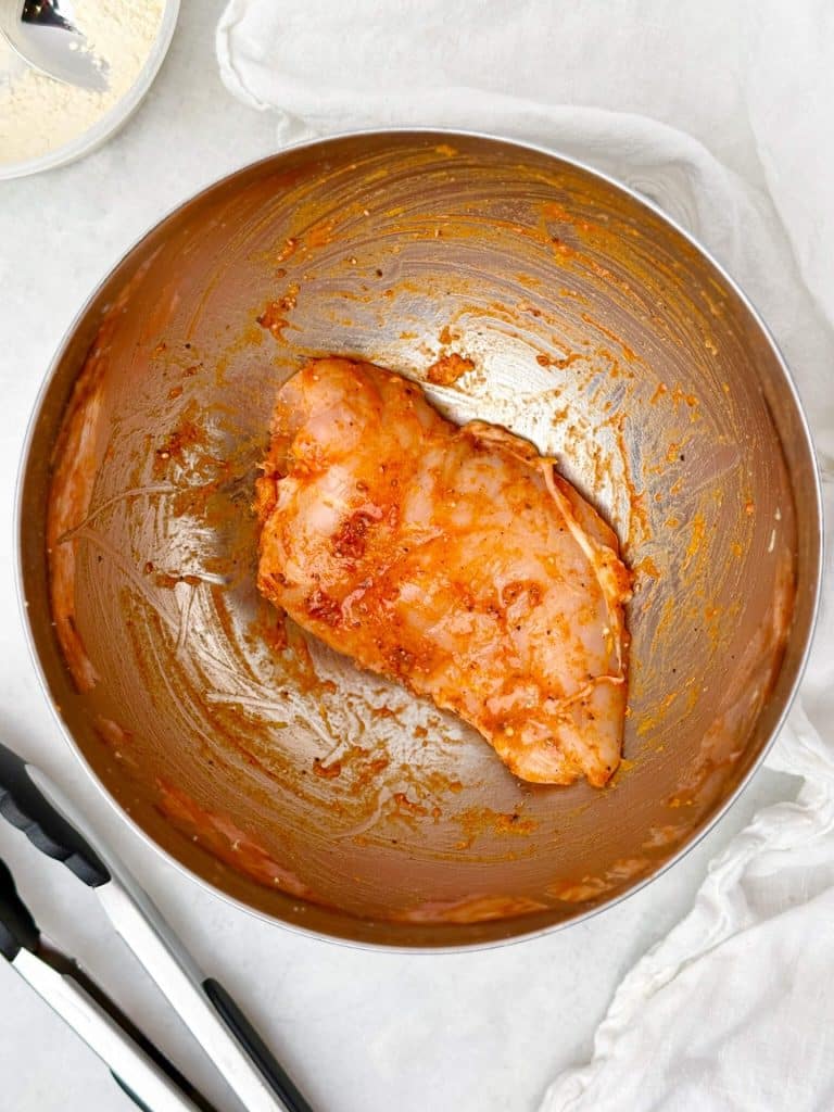 seasoned chicken breast in a bowl ready to cook for high protein chicken caesar wrap