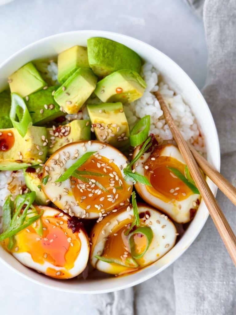 Close-up of soy sauce egg rice bowl with jammy yolk, avocado, and chili oil drizzle