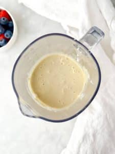 low carb cottage cheese pancake batter blended smooth in a blender jug with fresh berries in the background