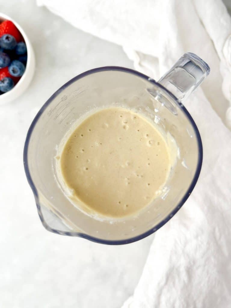 low carb cottage cheese pancake batter blended smooth in a blender jug with fresh berries in the background