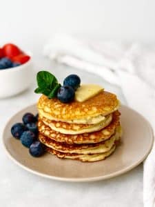 cottage cheese pancakes low carb served with a pat of butter and fresh blueberries on a beige plate