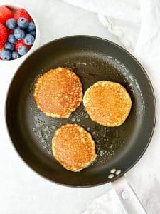 low carb cottage cheese pancakes cooking in a nonstick skillet until golden brown with fresh berries alongside