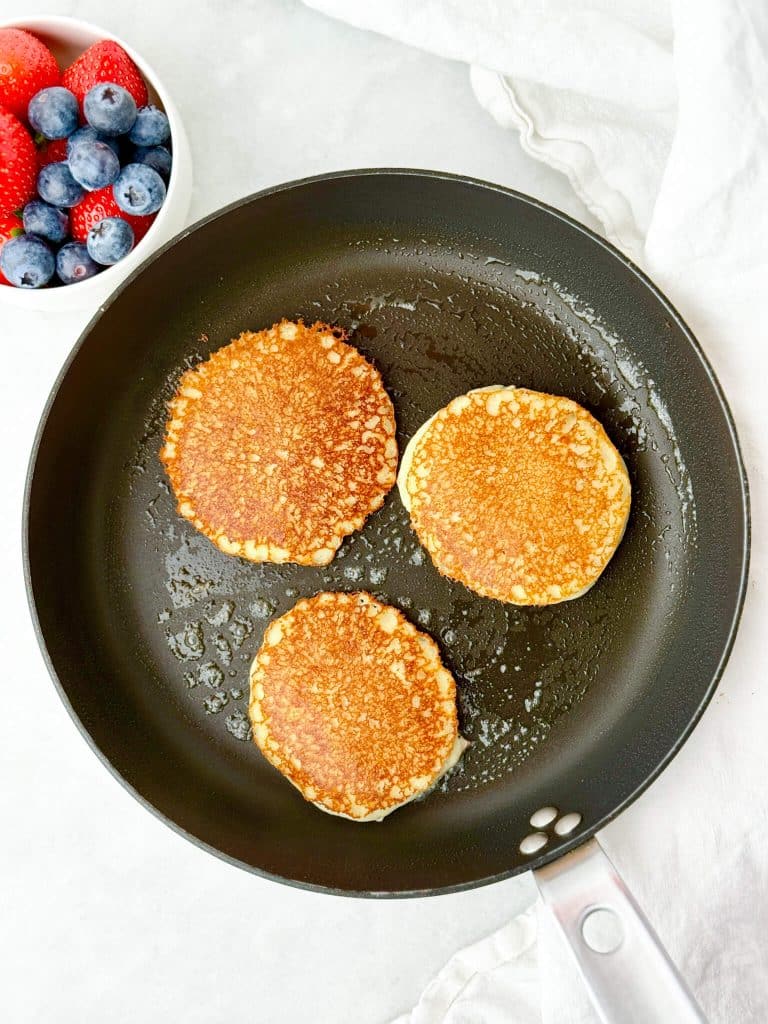 low carb cottage cheese pancakes cooking in a nonstick skillet until golden brown with fresh berries alongside