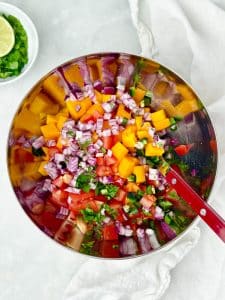 Fresh mango salsa with diced mango, tomato, red onion, jalapeño, and cilantro in a mixing bowl