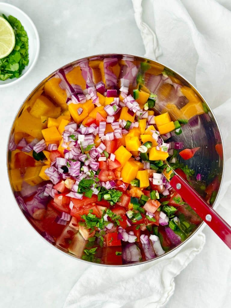 Fresh mango salsa with diced mango, tomato, red onion, jalapeño, and cilantro in a mixing bowl