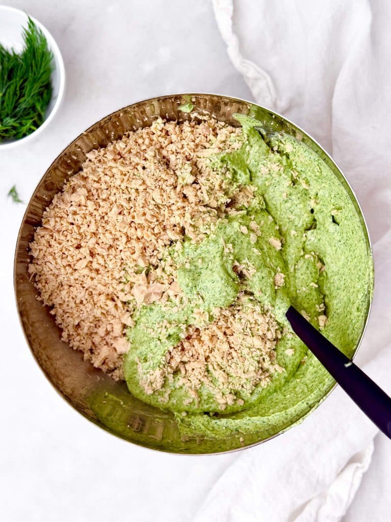 Shredded chicken being mixed with green goddess dressing in a metal mixing bowl