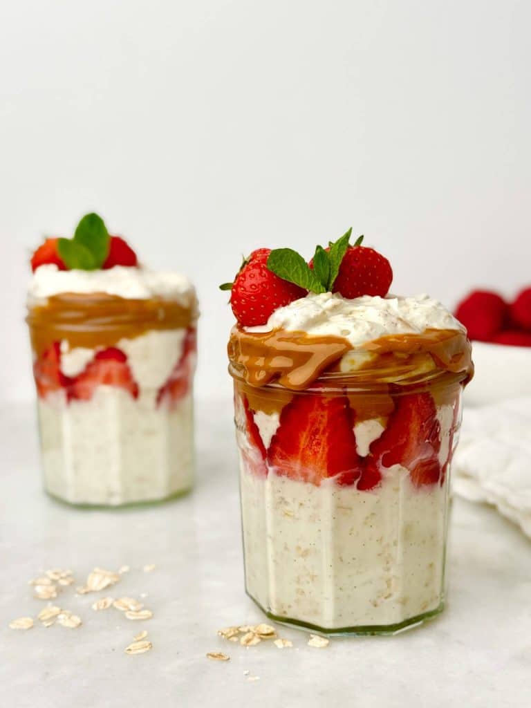Close-up of a high-protein yogurt parfait with oats in a glass jar, layered with fresh strawberries and creamy peanut butter, with rolled oats scattered on the surface.