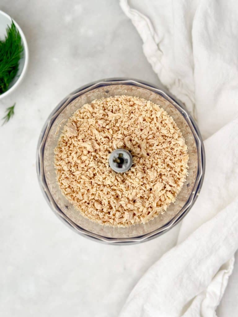 Finely shredded rotisserie chicken in a food processor bowl, fluffy texture with fresh dill in the background