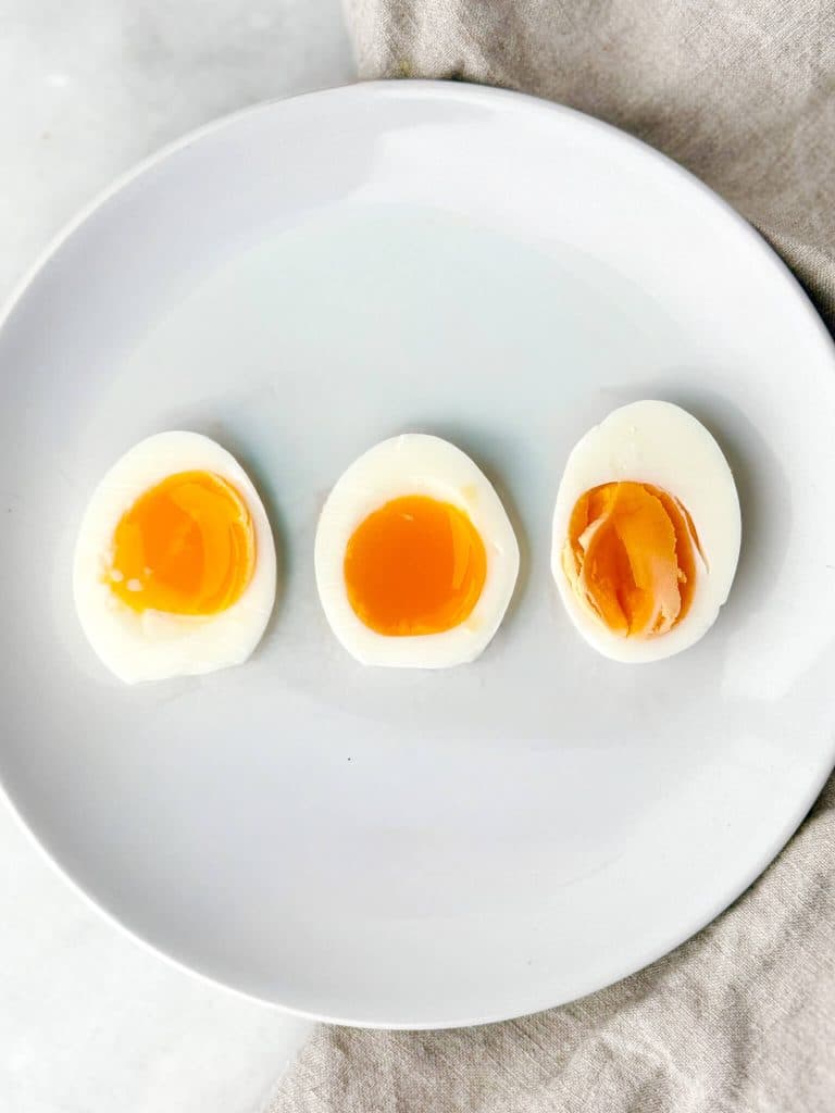 Three halved soft-boiled eggs on a white plate showing 6, 7, and 8 minute cook times