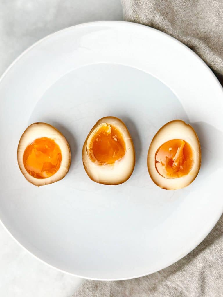 Three halved soy marinated eggs on a white plate showing 6, 7, and 8 minute yolk textures