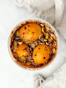 Soy marinated eggs in a container with sesame seeds, green onion, and chili oil