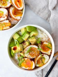 Two soy sauce egg rice bowls with halved jammy eggs, avocado, and chopsticks
