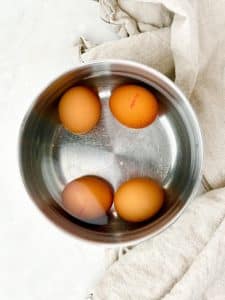 Four brown eggs in a stainless steel pot of water before boiling