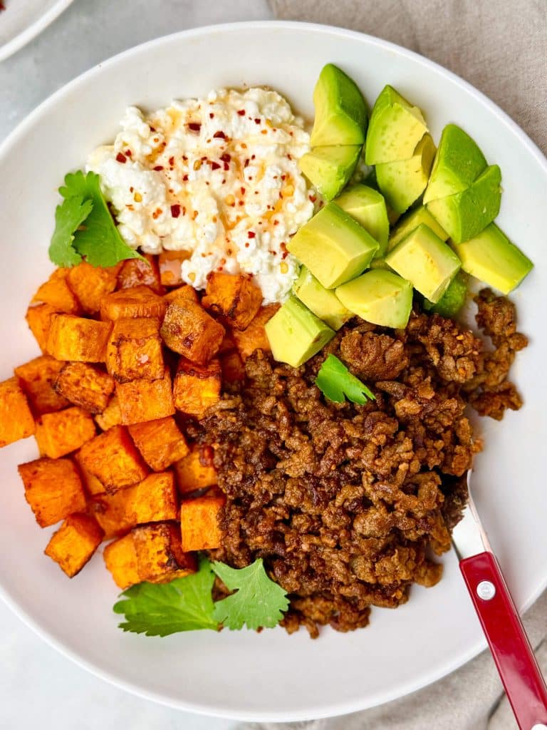 Viral high protein taco bowl with roasted sweet potato, taco-seasoned ground beef, cottage cheese, diced avocado, and fresh cilantro